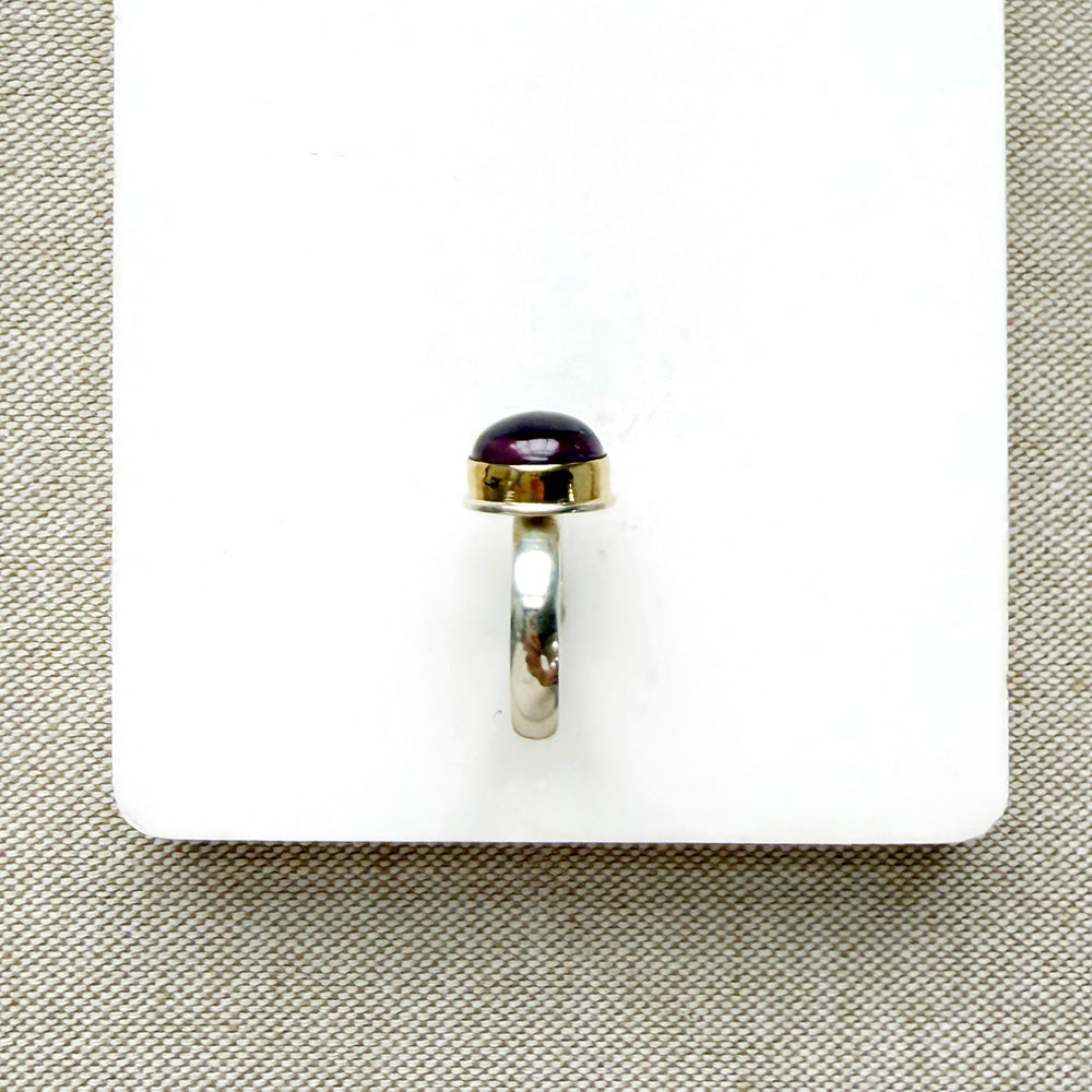 side view of round smooth cut mauve spinel ring on a white dish