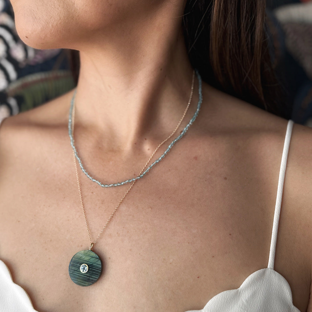 Close up of woman wearing a labradorite pendant with small inset blue quartz stone on a gold chain