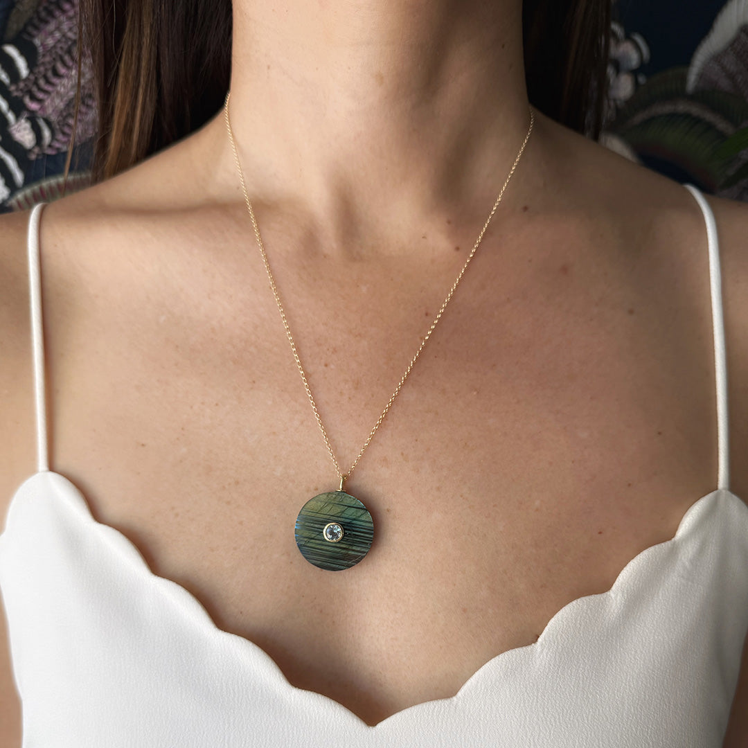 Close up of woman wearing a labradorite pendant with small inset blue quartz stone on a gold chain