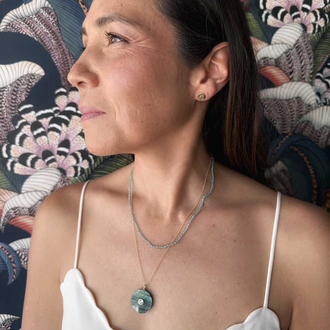Close up of woman wearing a labradorite pendant with small inset blue quartz stone on a gold chain