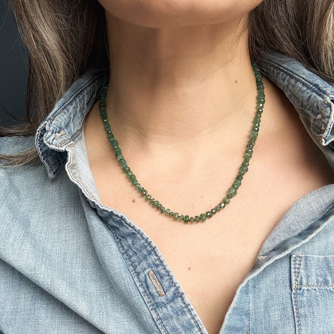 Person wearing a green gemstone necklace with a denim shirt