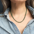 Person wearing a green gemstone necklace with a denim shirt