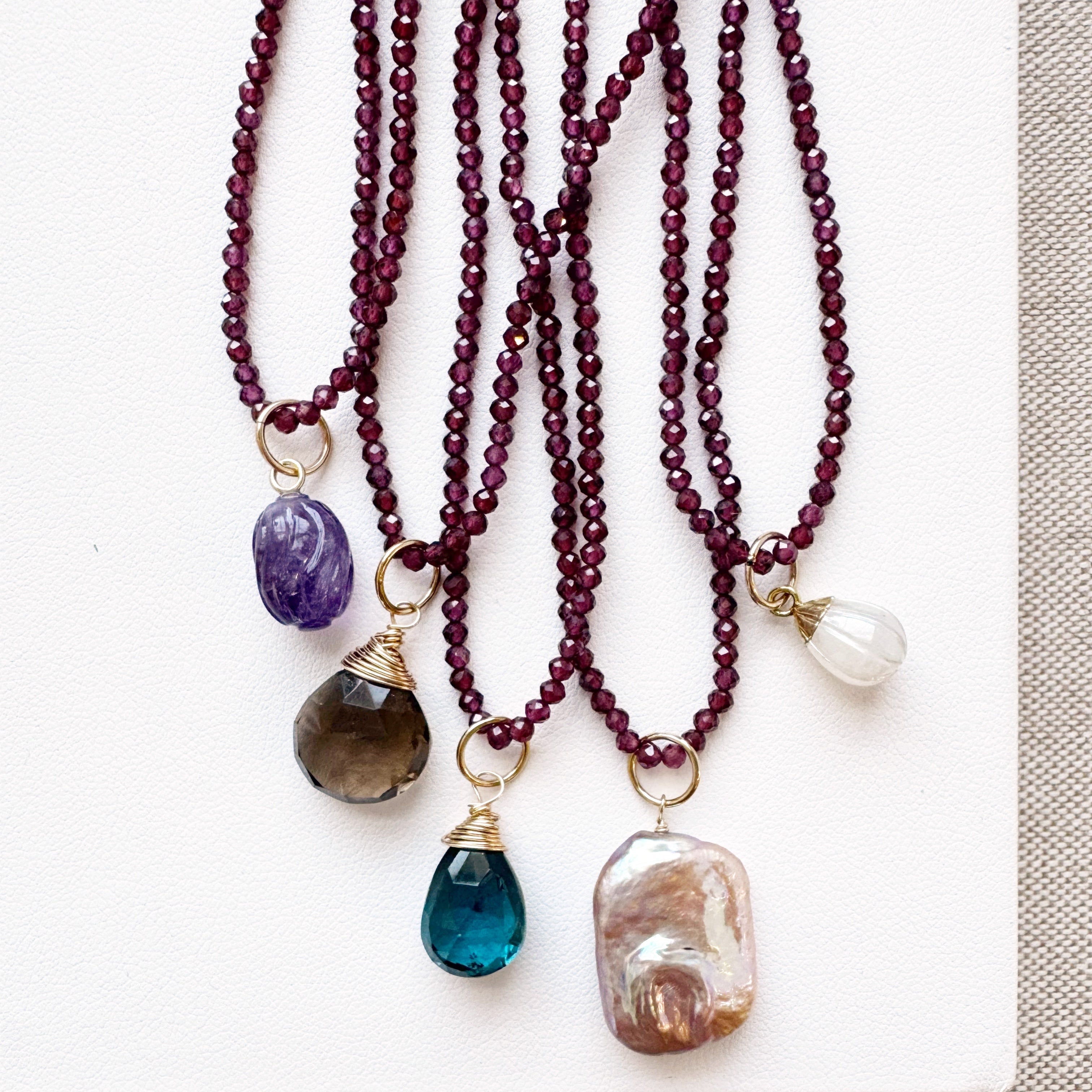 Three beaded necklaces with various colored stone pendants on a white surface.