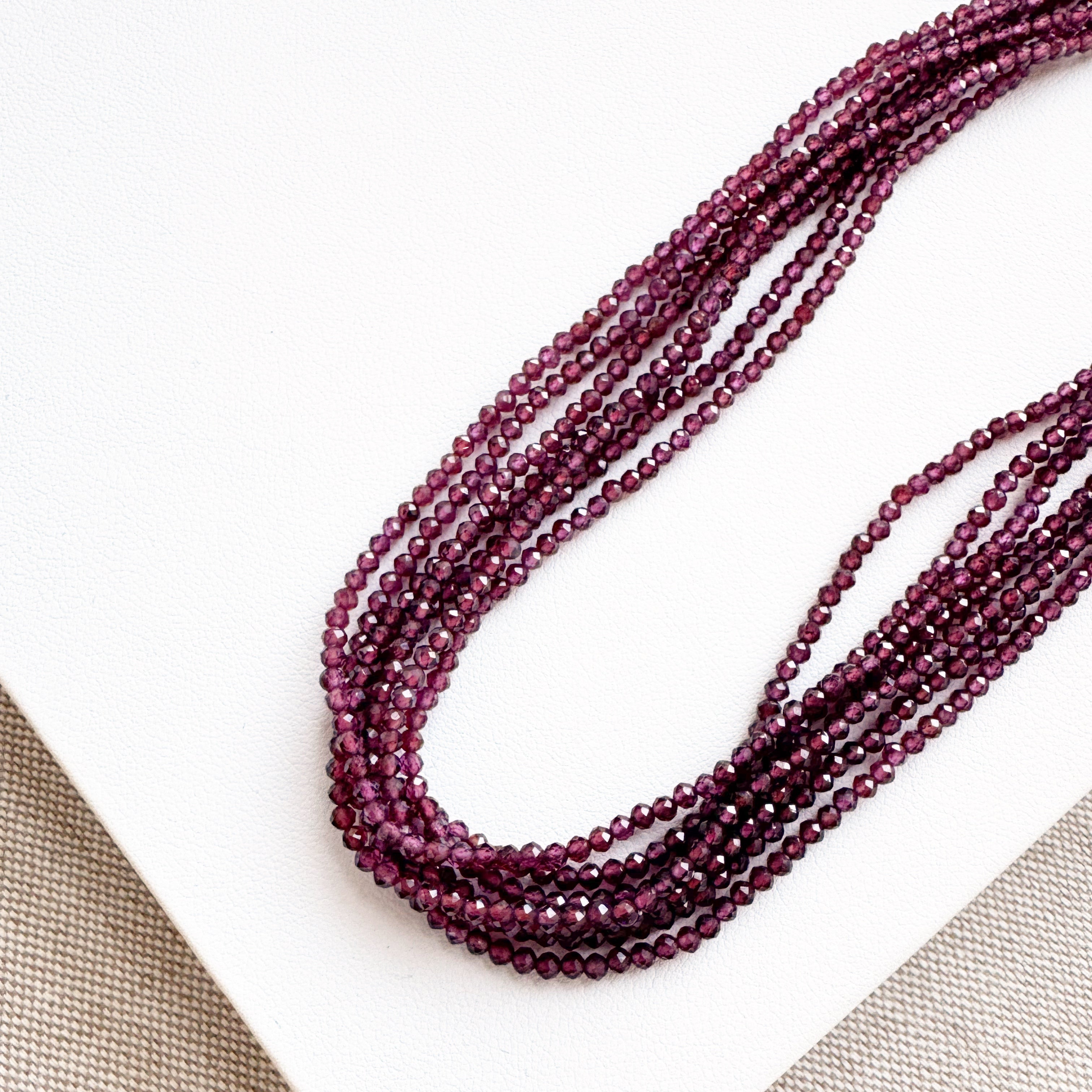 Beaded necklace in purple on a white surface with a beige fabric background