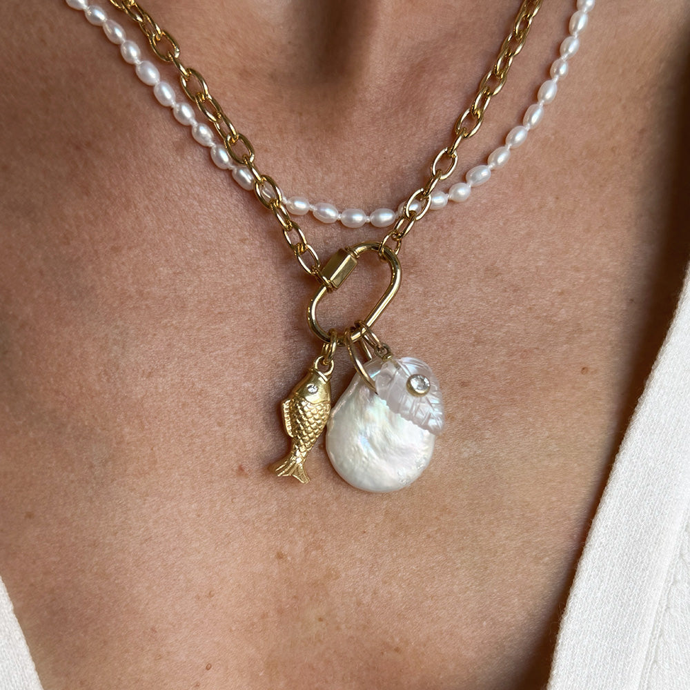 A close-up of a woman wearing a gold chain with a charm carabiner and mixed charms