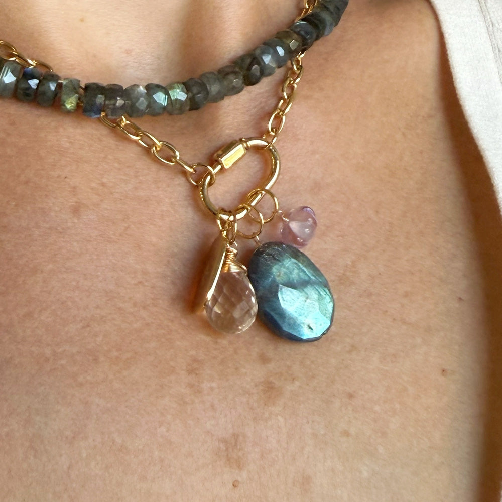 A close-up of a woman wearing a gold chain with a charm carabiner and mixed charms