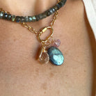 A close-up of a woman wearing a gold chain with a charm carabiner and mixed charms