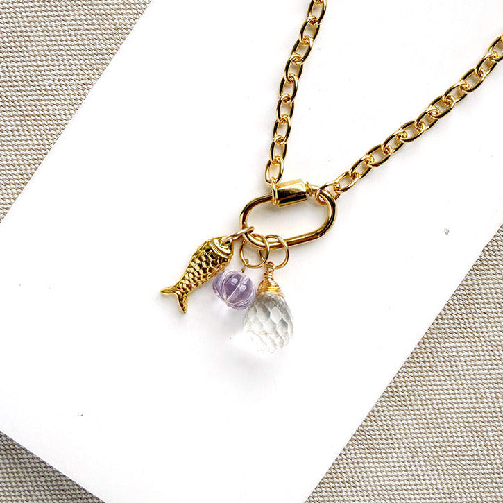 A gold chain with a charm carabiner and mixed charms on white background