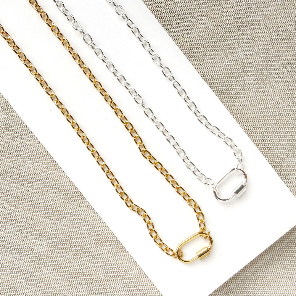 Two chain necklaces, one gold-toned and one silver-toned, displayed on a white rectangular card over a textured beige fabric background.