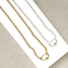 Two chain necklaces, one gold-toned and one silver-toned, displayed on a white rectangular card over a textured beige fabric background.