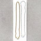 Two chain necklaces, one gold and one silver, displayed on a white rectangular card against a textured gray fabric background.