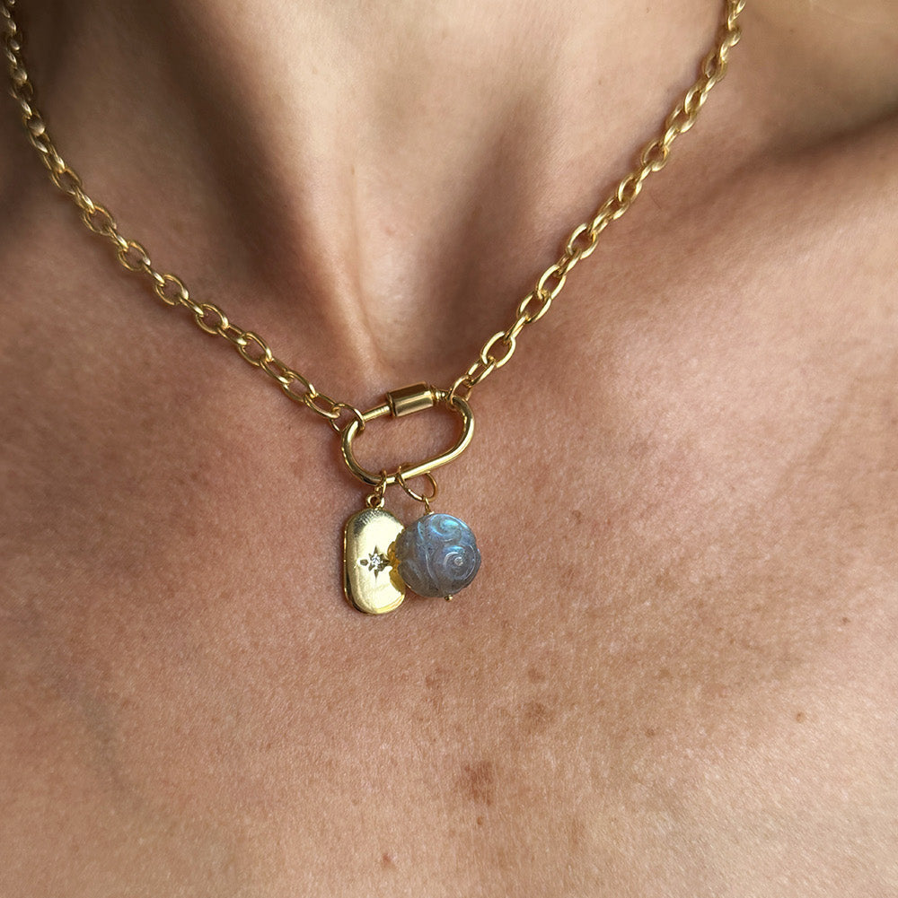 A close-up of a gold chain necklace worn on a person's neck, featuring a small gold tag charm with a star and carved labradorite charm