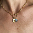 A close-up of a gold chain necklace worn on a person's neck, featuring a small gold tag charm with a star and carved labradorite charm