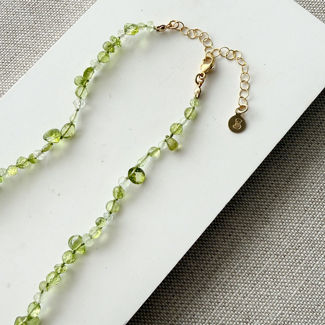 Gemstone necklace in shades of green on a white card with a gold clasp