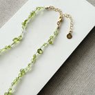 Gemstone necklace in shades of green on a white card with a gold clasp