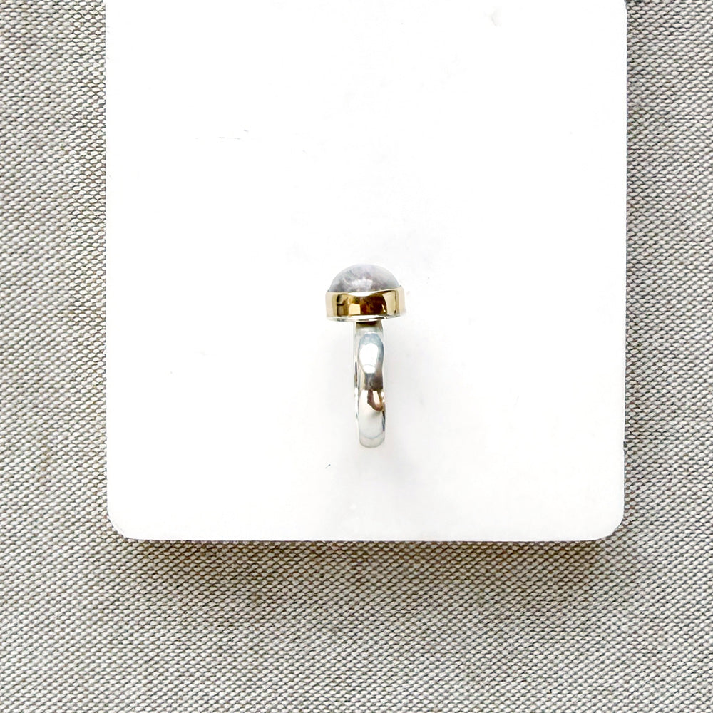 Side view of round moonstone mixed metal ring on a white background