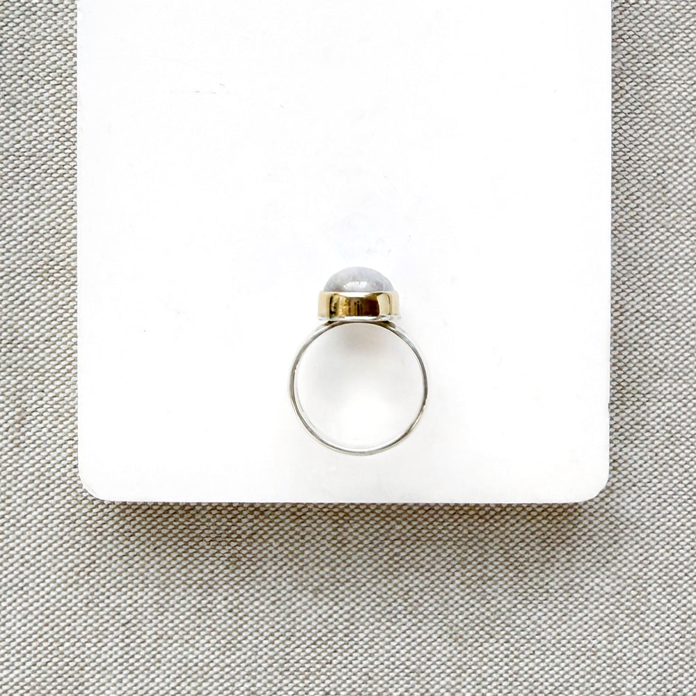 Side view of round moonstone mixed metal ring on a white background