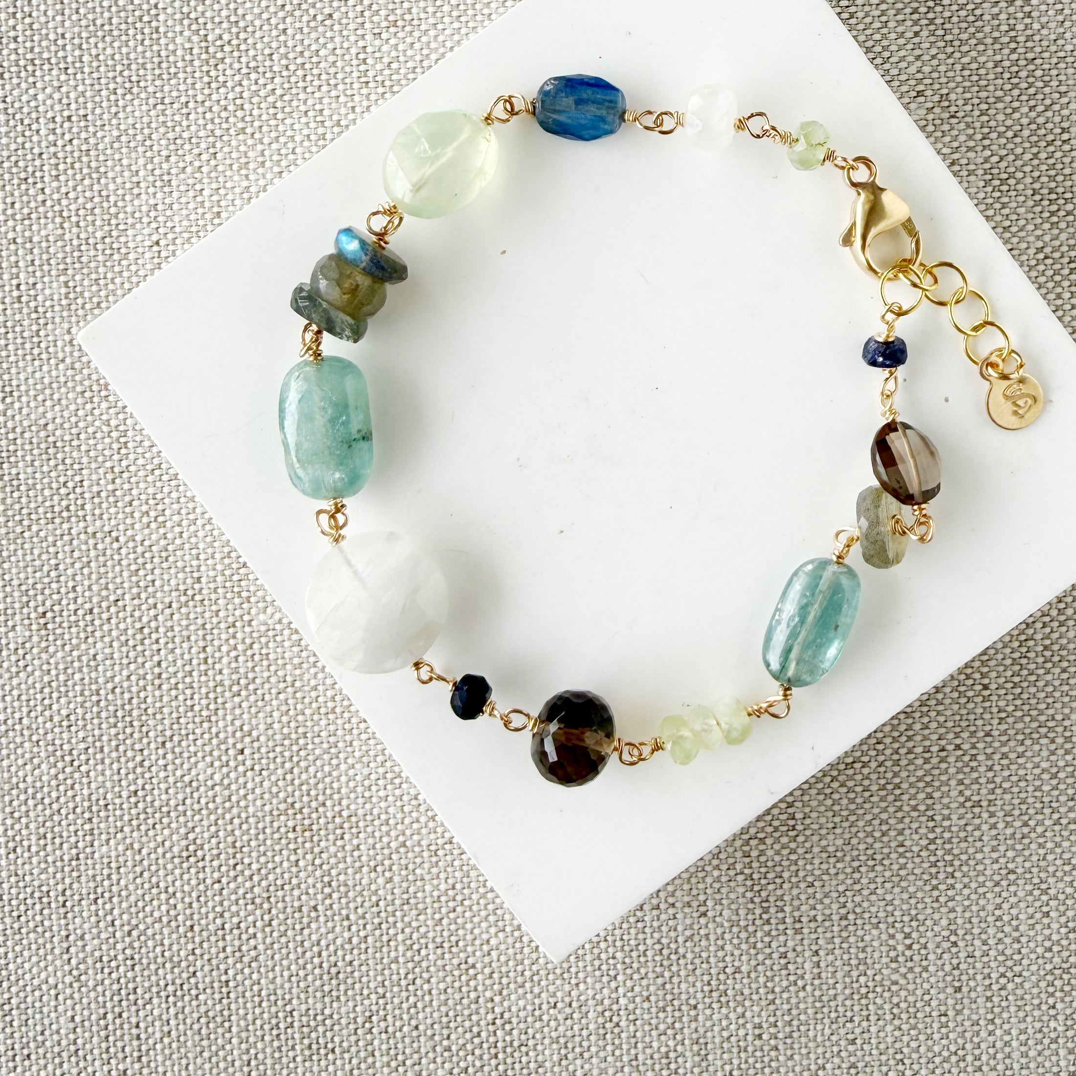 Multicolored chunky gemstone bracelet on a white square card with a textured beige background