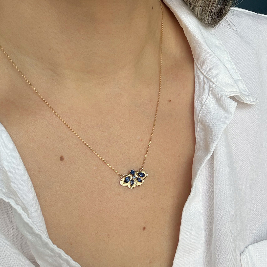 Gold necklace with a moth pendant worn by a person in a white shirt.