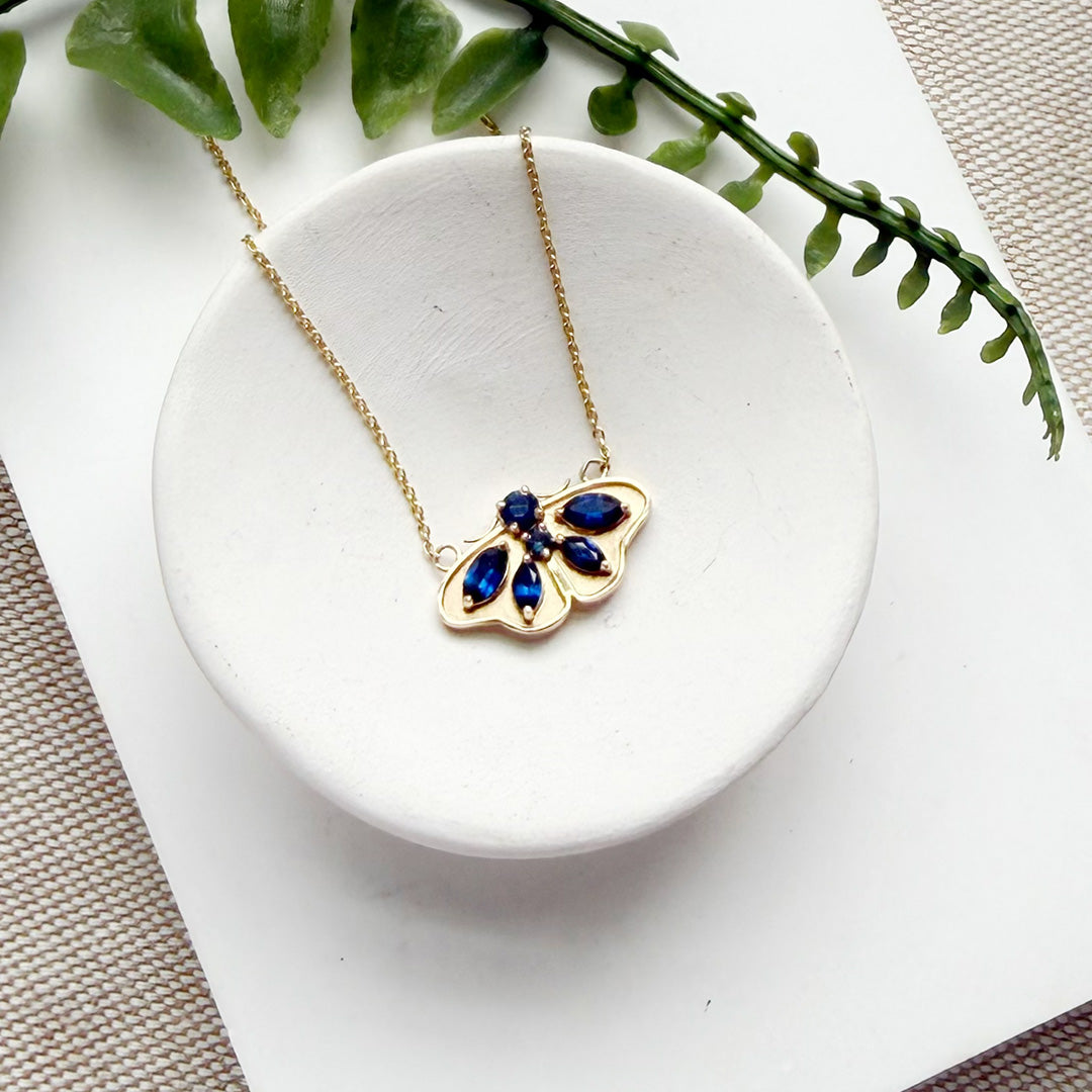 Close up of gold pendant in the shape of a moth, set with sapphires