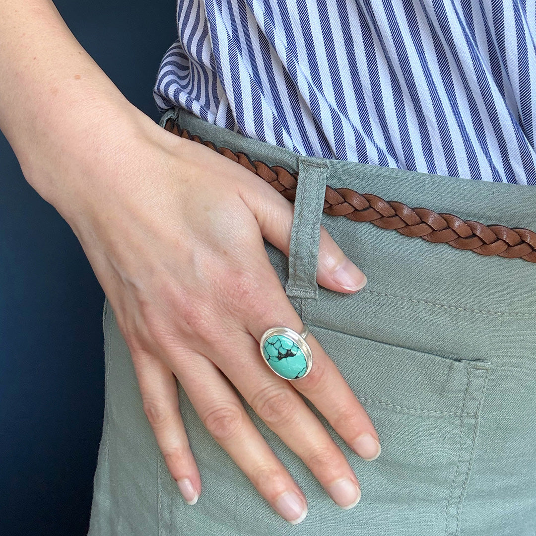 Close up of woman wearing Nevada turquoise ring against a blue background