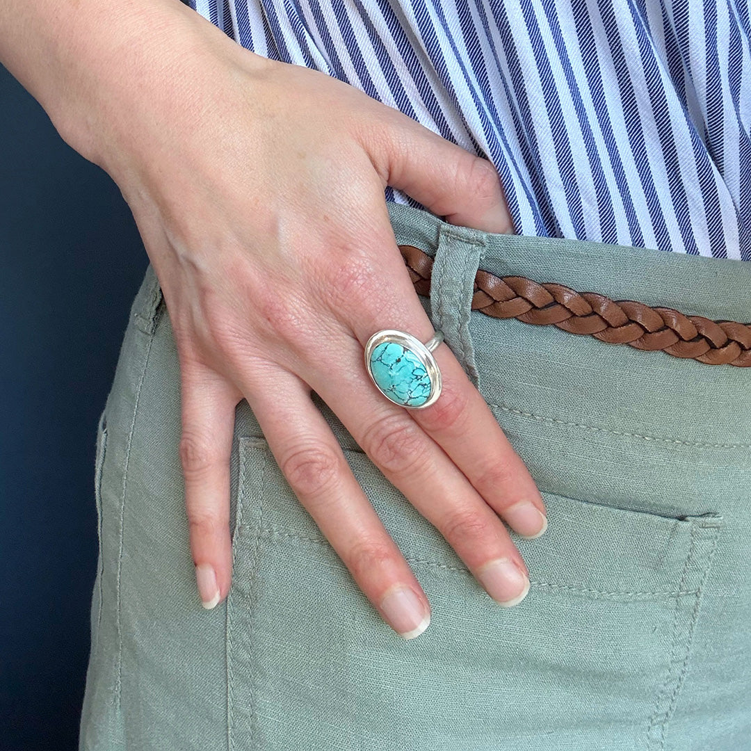 Close up of woman wearing Nevada turquoise ring against a blue background