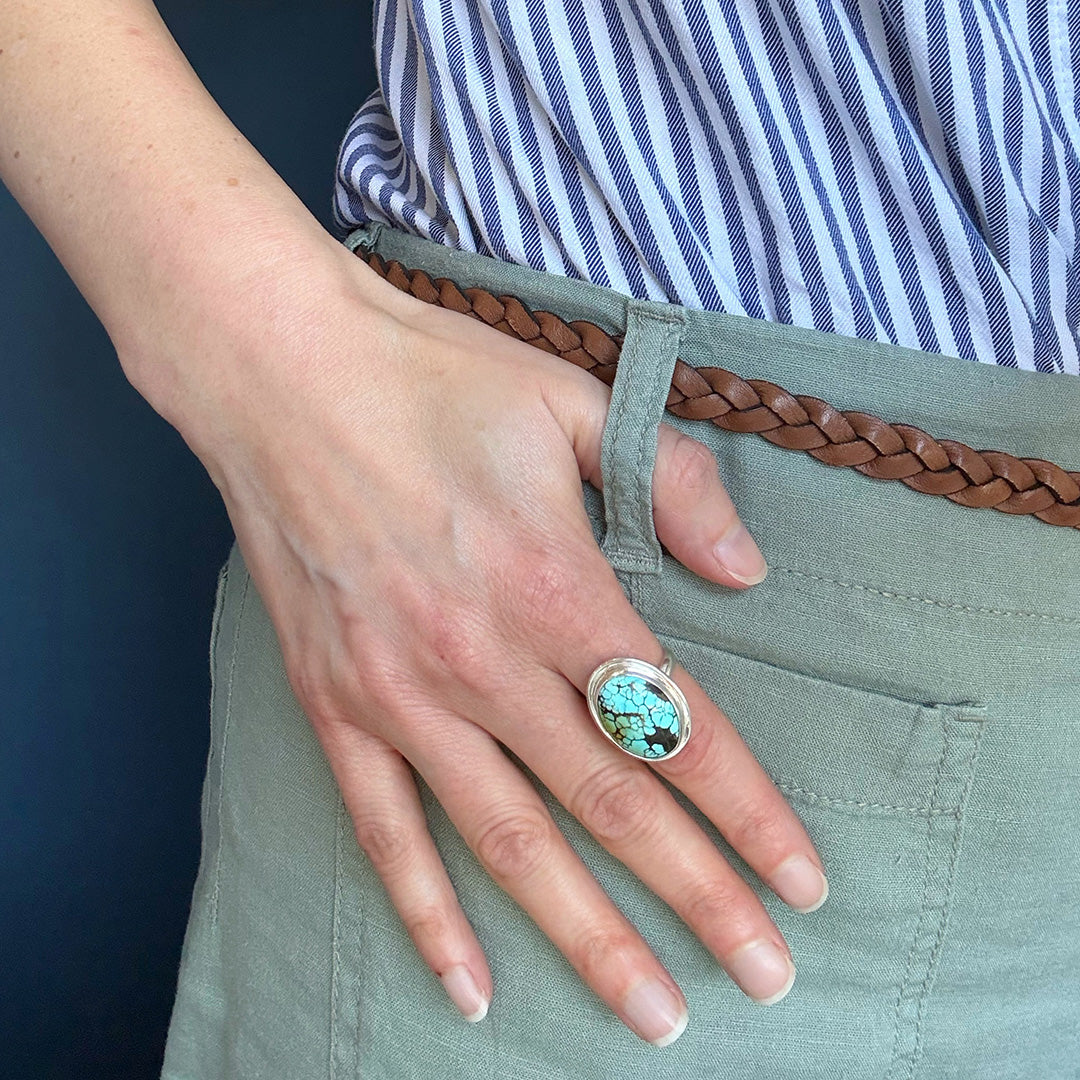 Close up of woman wearing Nevada turquoise ring against a blue background