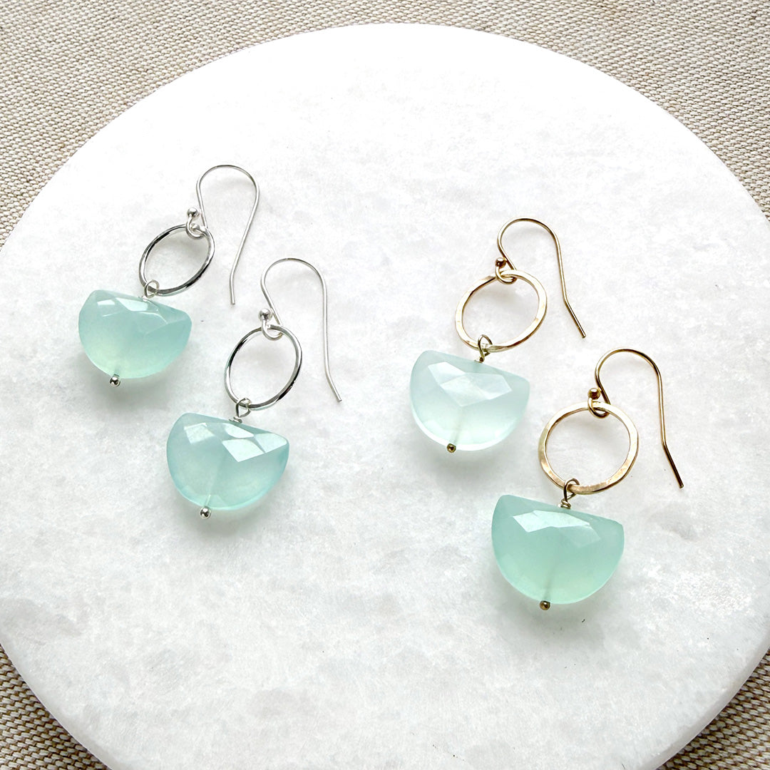 Pair of earrings with blue chalcedony gemstones in a half moon shape on a white stone surface