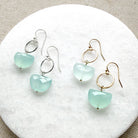 Pair of earrings with blue chalcedony gemstones in a half moon shape on a white stone surface