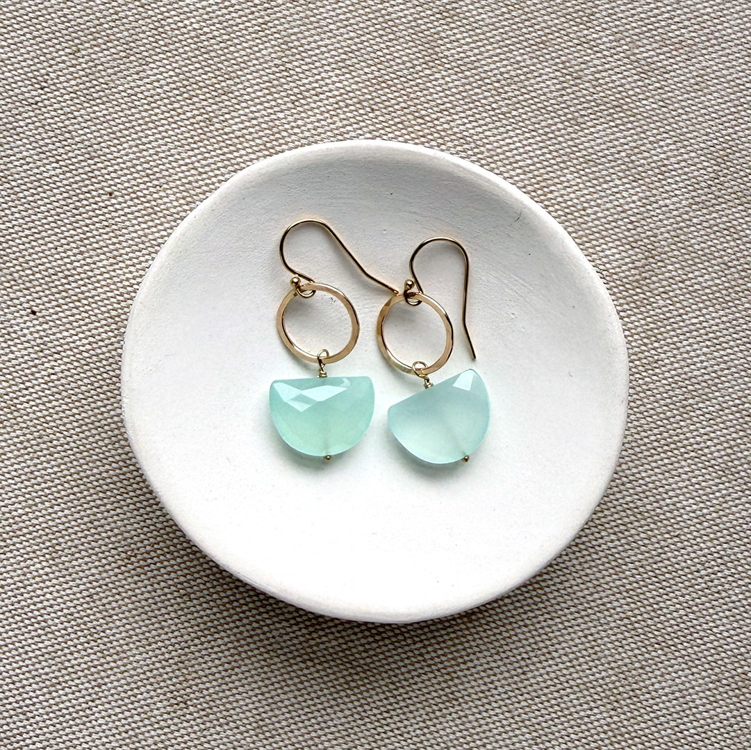 Pair of earrings with blue chalcedony stones on a white dish against a beige background