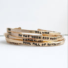 Stack of gold bracelets with engraved text on a white background