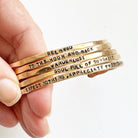 Gold bracelets with motivational phrases held by a hand on a white background