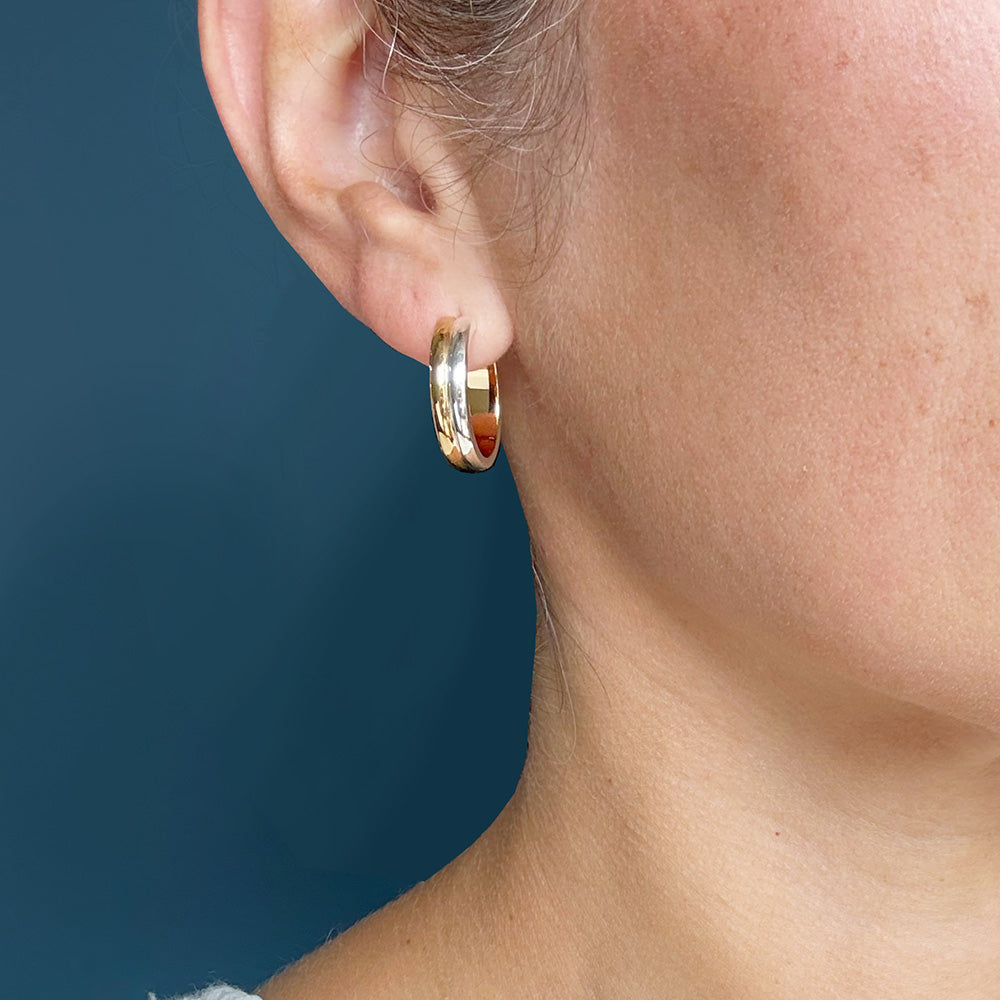 A close-up side view of a person's ear wearing a polished gold and silver hoop earring against a dark blue background.