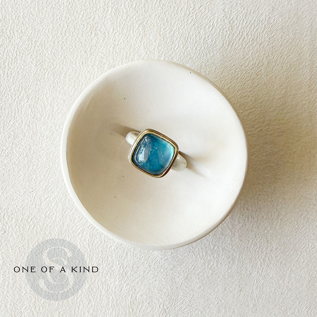 Smooth cushion cut aquamarine ring in a white dish with one-of-a-kind branding