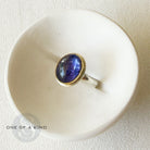 Ring with a purple tanzanite gemstone on a white dish, with 'One of a Kind' icon.