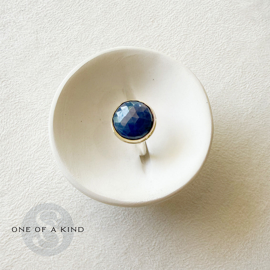 Round faceted sapphire ring in a white dish with one of a kind icon