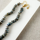 Clasp detail of a necklace with labradorite gemstones on a white dish against a beige fabric background