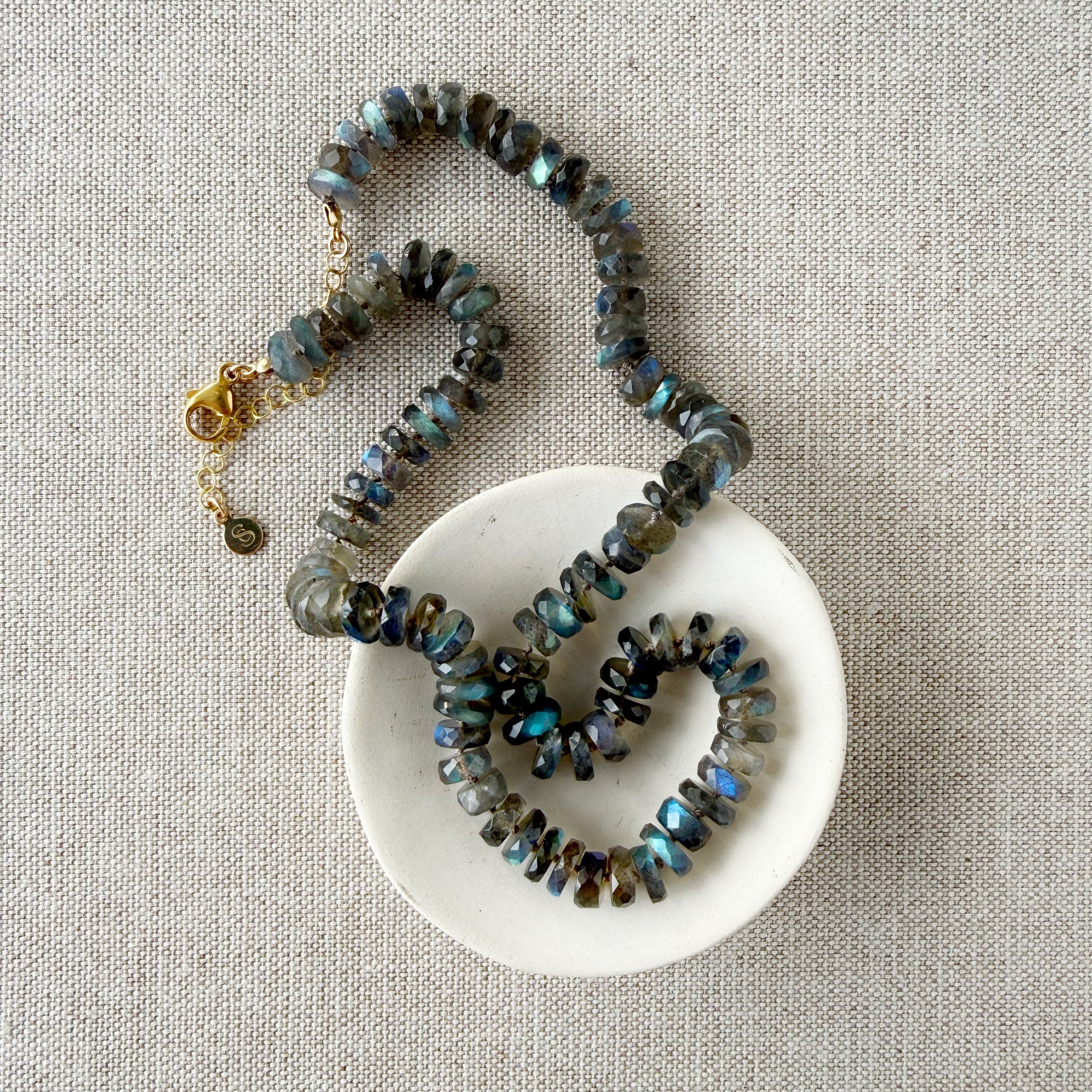 Necklace with labradorite gemstones on a white dish against a beige fabric background