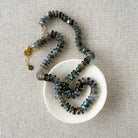 Necklace with labradorite gemstones on a white dish against a beige fabric background