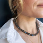 Close-up of a person wearing a labradorite gemstone necklace and earrings against a dark background