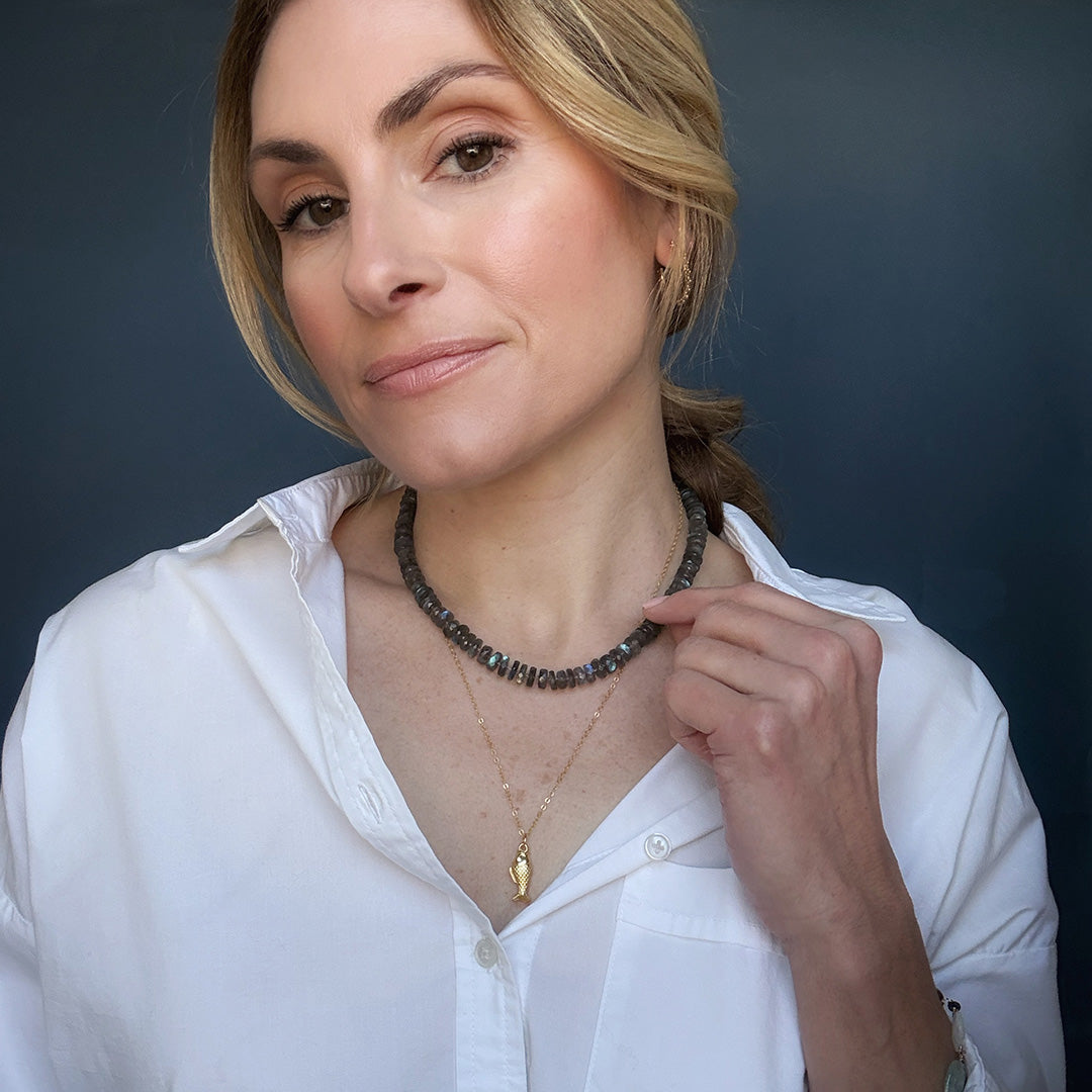 Woman wearing a labradorite gemstone necklace and sardine pendant against a dark background