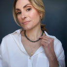 Woman wearing a labradorite gemstone necklace and sardine pendant against a dark background