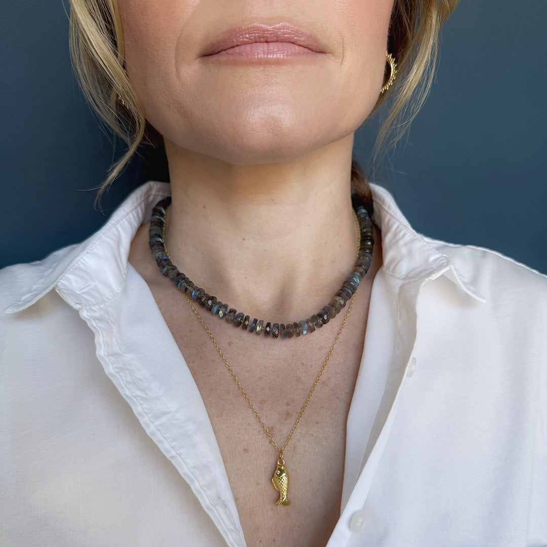 Woman wearing a labradorite gemstone necklace and sardine pendant against a dark background