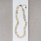 Chunky gold chain necklace on a white card with a gray background