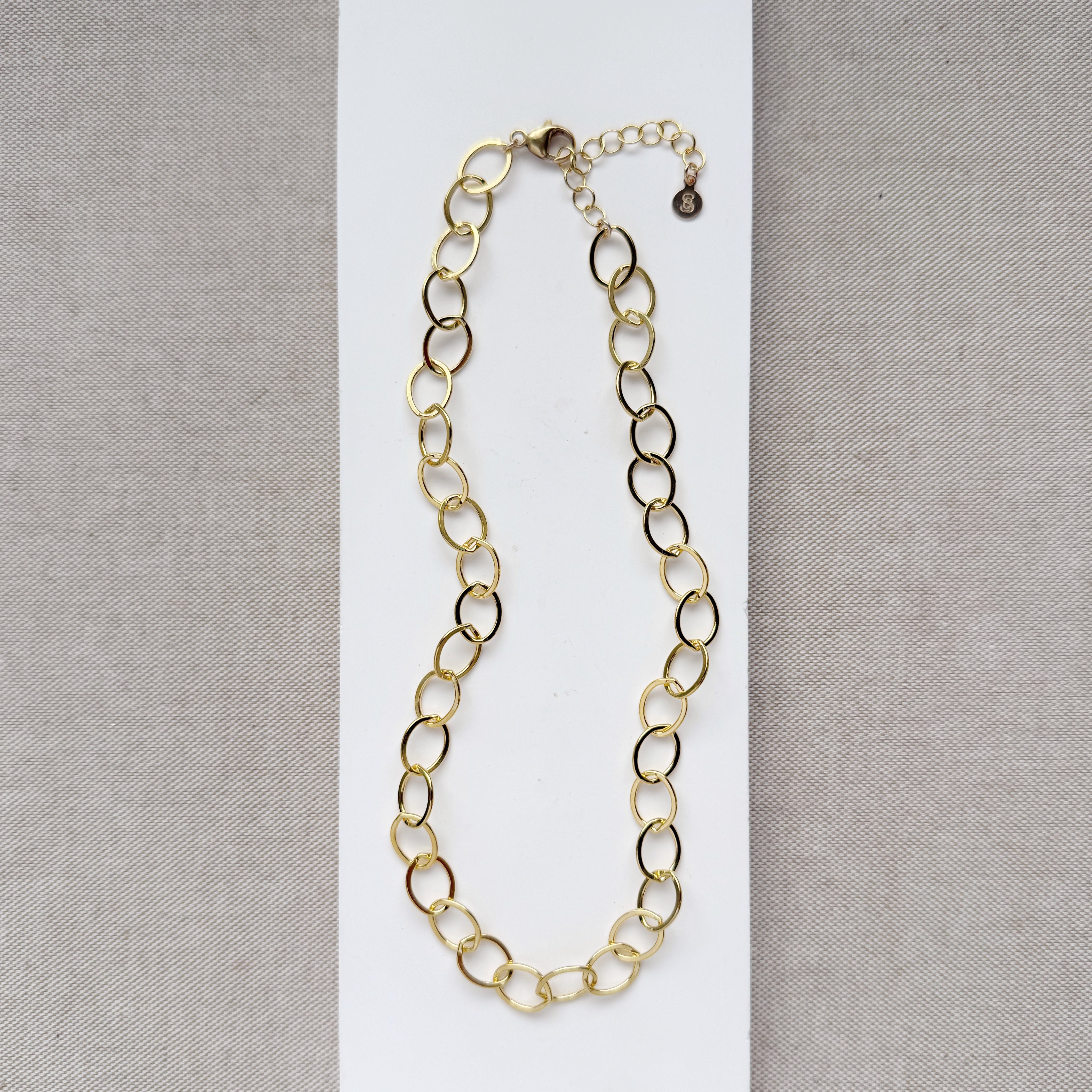 Chunky gold chain necklace on a white card with a gray background