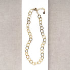 Chunky gold chain necklace on a white card with a gray background