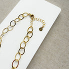Chunky gold chain necklace on a white card with a gray background