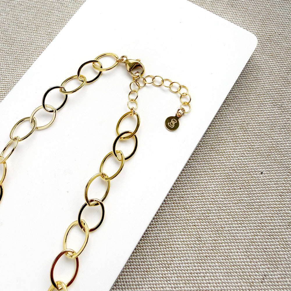 Chunky gold chain necklace on a white card with a gray background