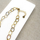 Chunky gold chain necklace on a white card with a gray background