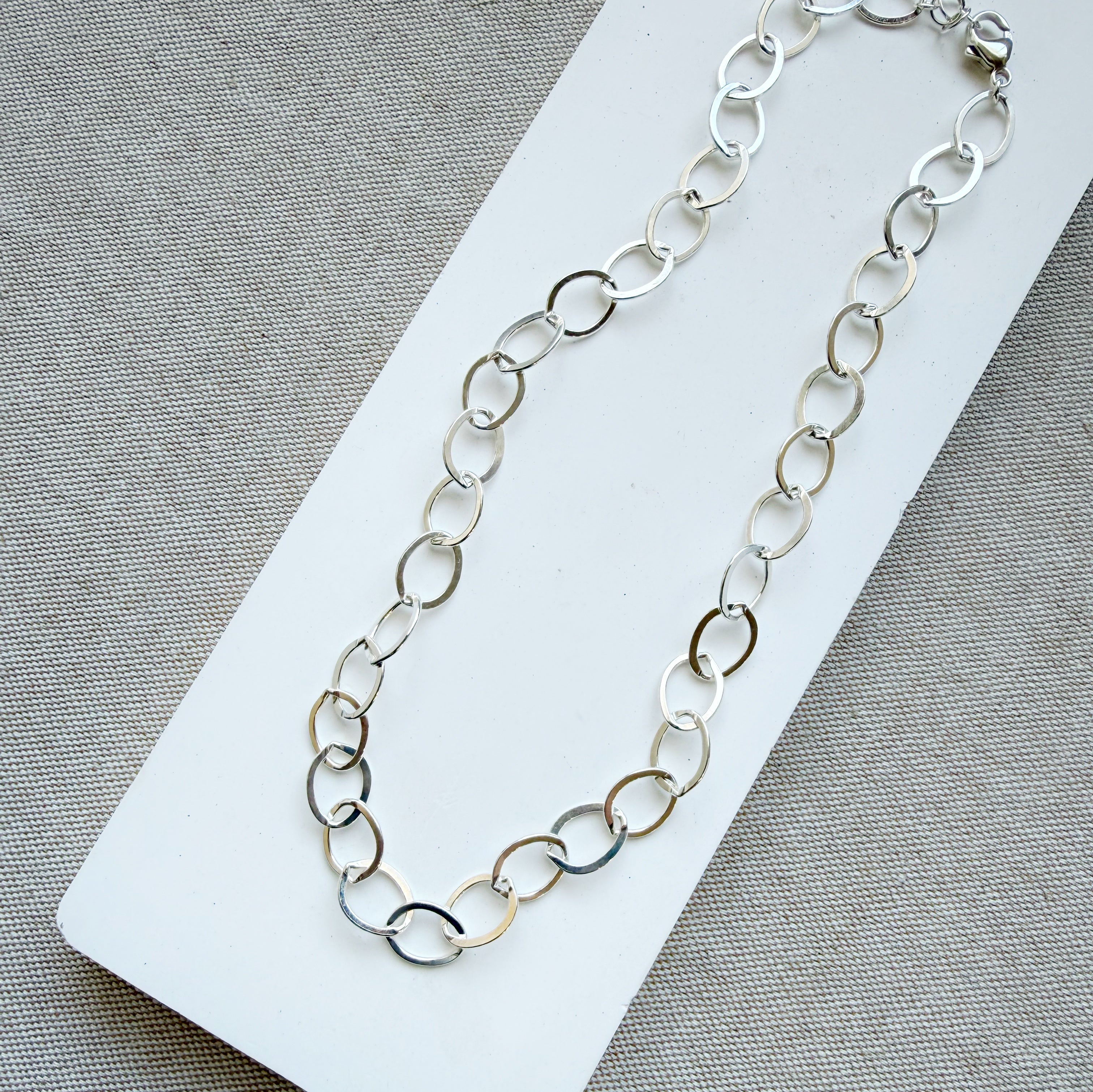 Chunky silver chain necklace on a white card with a gray background
